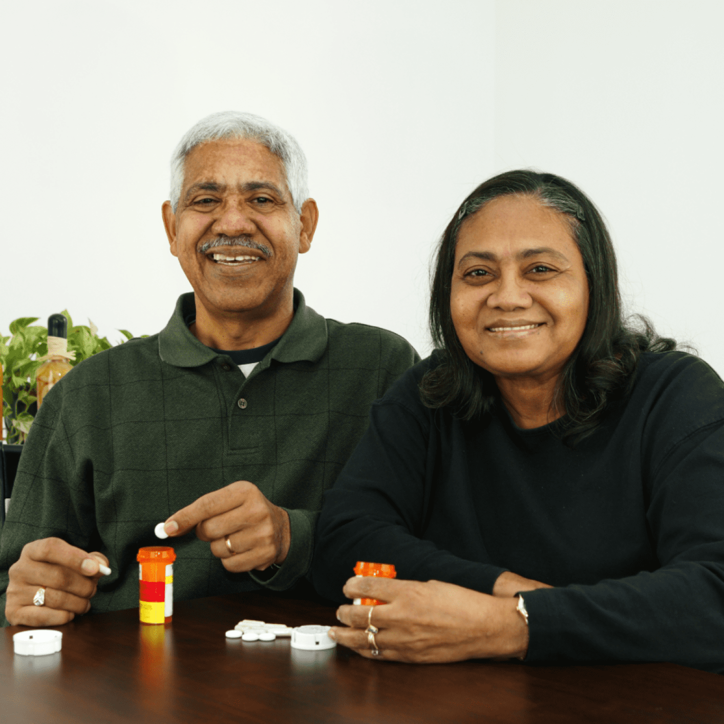 A couple holding their medication bottles, smiling at the camera.