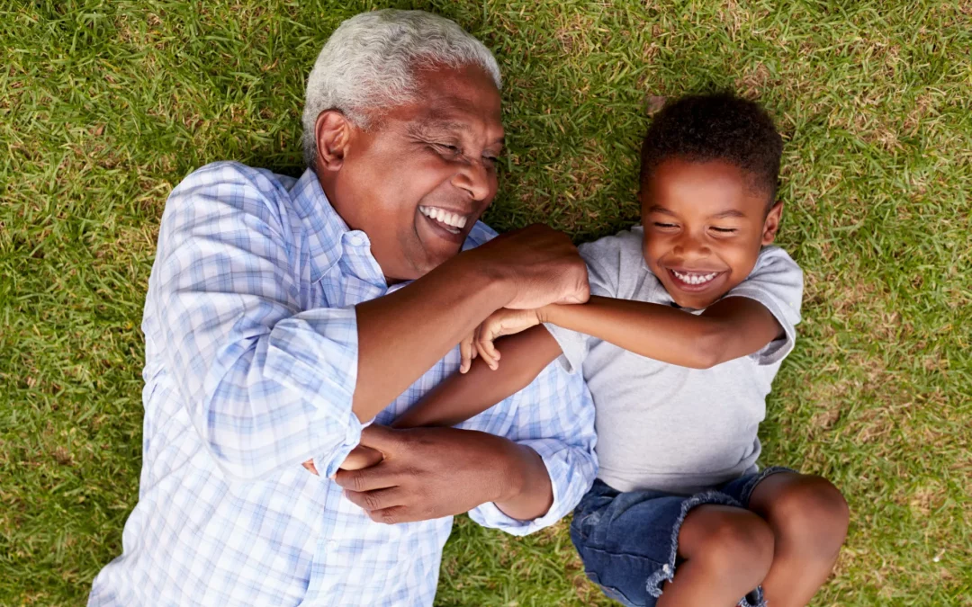 A photo of a grandpa and his grandson lying in the grass smiling and laughing.
